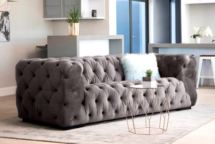 Velvet grey, buttoned couch on light grey rug in modern living room